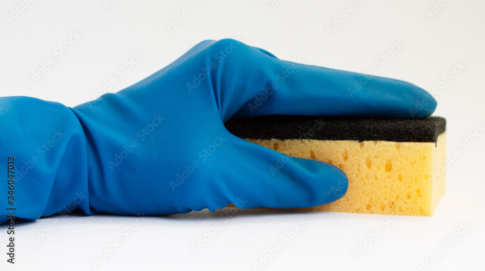 a woman's hand in a blue rubber glove holds a clean new dishwashing sponge on a white background a woman's hand in a blue rubber glove holds a clean new dishwashing sponge on a white background