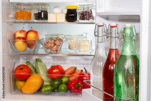 Refrigerador abiero con alimentos y bebidas en recipientes de vidrio, libre de plásticos