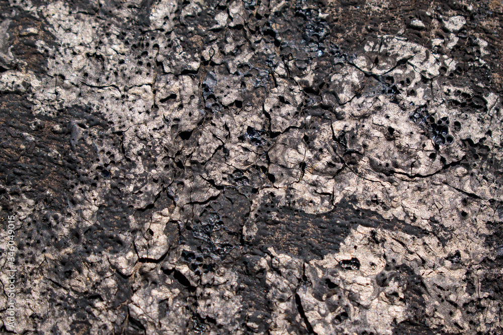 Wall with old tar for backdrop. Dark and light areas of gray. Flaking, cracks, potholes and craters. Wall with old tar for backdrop. Dark and light areas of gray. Flaking, cracks, potholes and craters.
