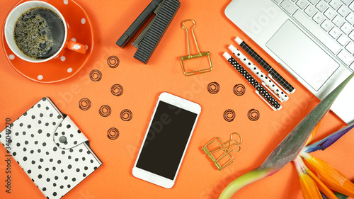 Desktop workspace flat lay with hi-tech touch screen laptop and modern orange, black and white accessories on orange trend background.