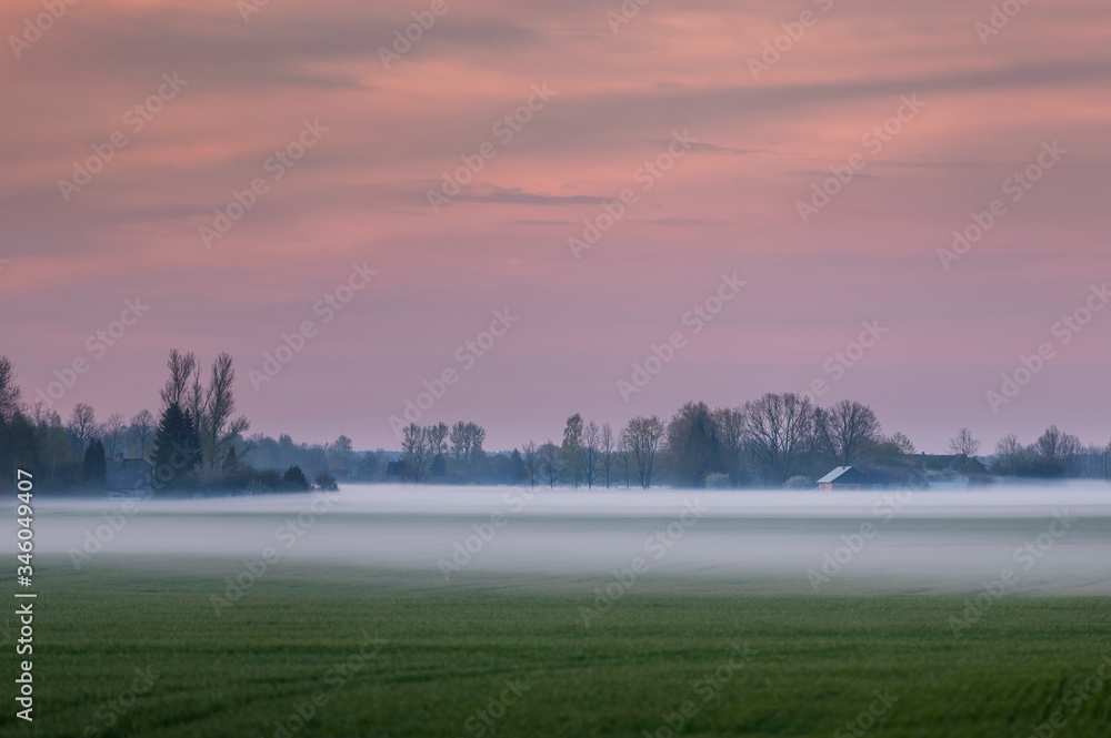 Fototapeta premium Fog layers over agricultural field during spring sunset (high ISO image)