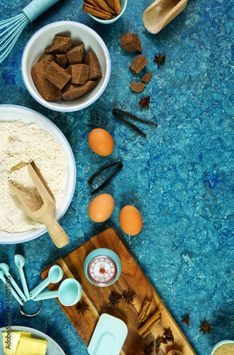 Baking flatlay creative composition top view for chocolate recipes including eggs, flour, butter and spices, with cooking accessories on vintage textured blue background table. Vertical orientation.