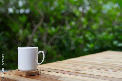cup of coffee on a wooden table at green tree background