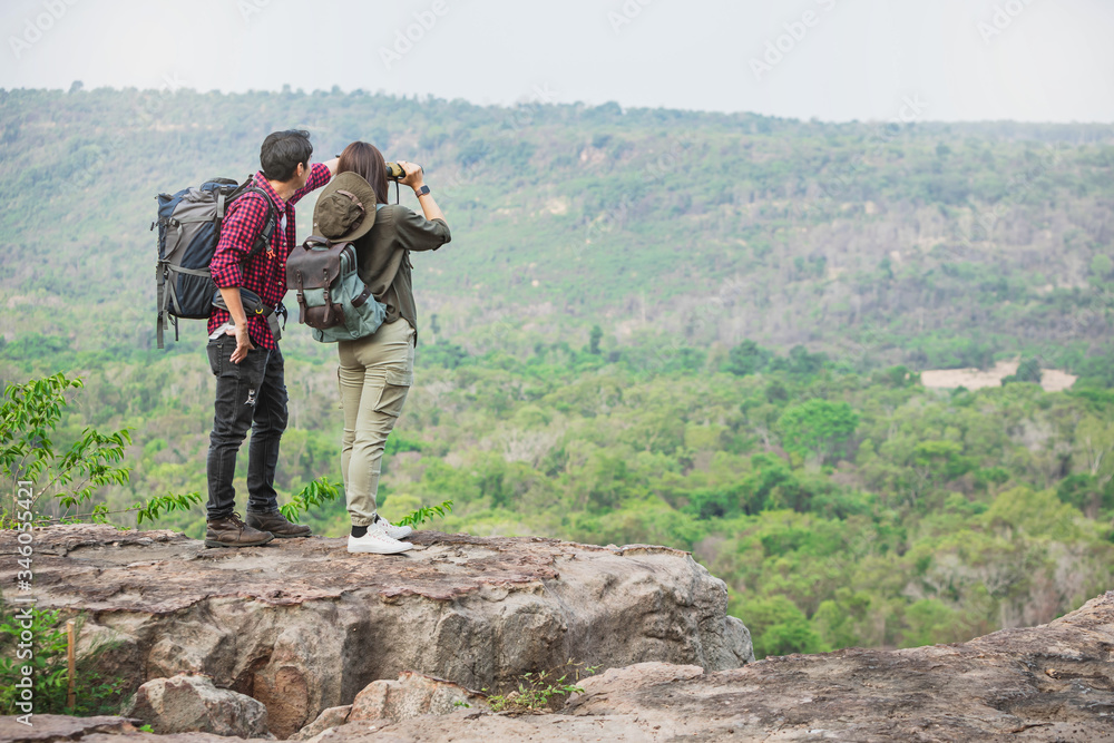 Traveler couple in love enjoying view of beautiful panorama of the wild and holding hands each other. Hikers with backpacks relaxing on top of a hill and enjoying view of sunset .