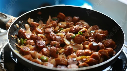 Frying hot sausages with chillies in a black pan.