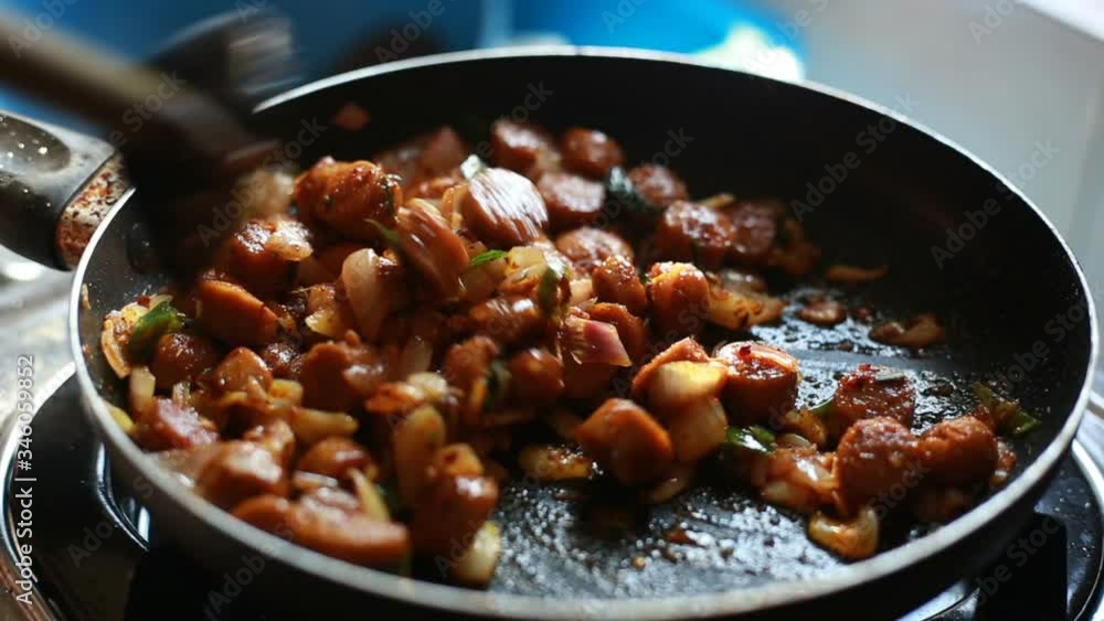 Frying hot sausages mix with chillies and stiring in a black pan.