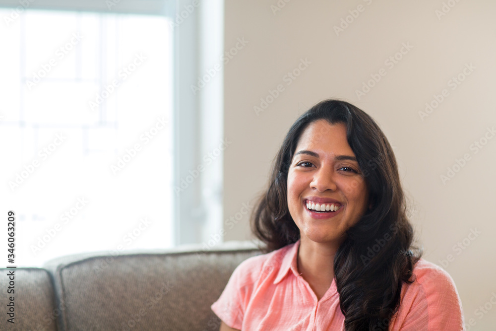 Young Hispanic woman smiling sitting on a sofa. - obrazy, fototapety, plakaty 
