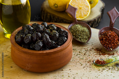 Black olives marinated with seasoning in caserolle bowl on wood block with lemon,seasoning and olive oil bottle. photo