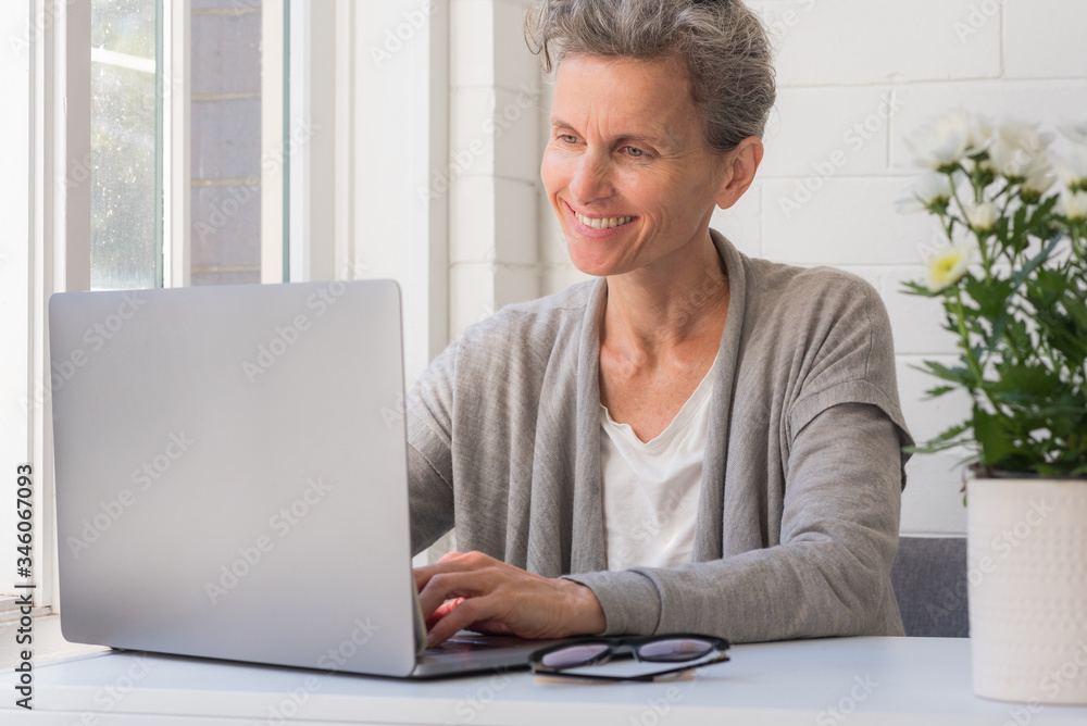 Close up of middle age woman smiling and using laptop - working from home concept (selective focus) Close up of middle age woman smiling and using laptop - working from home concept (selective focus)