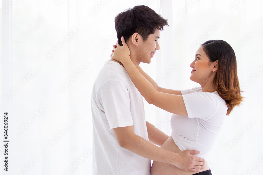 Asian lovely husband and wife portrait, his wife is in pregnancy. Husband tenderly hug and kiss his wife on the bed with care. Husband embracing his pregnant wife and making their hands in heart shape Asian lovely husband and wife portrait, his wife is in pregnancy. Husband tenderly hug and kiss his wife on the bed with care. Husband embracing his pregnant wife and making their hands in heart shape