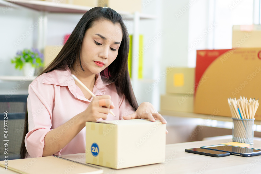 Young Asian business woman packing a post boxes to be shipped to customers. Ecommerce online shopping concept. Expertise online sales person packing customers parcel boxes for shipment. Young Asian business woman packing a post boxes to be shipped to customers. Ecommerce online shopping concept. Expertise online sales person packing customers parcel boxes for shipment.