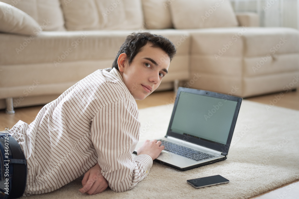 Naklejka premium Teenager young man lying on carpet and using laptop at home