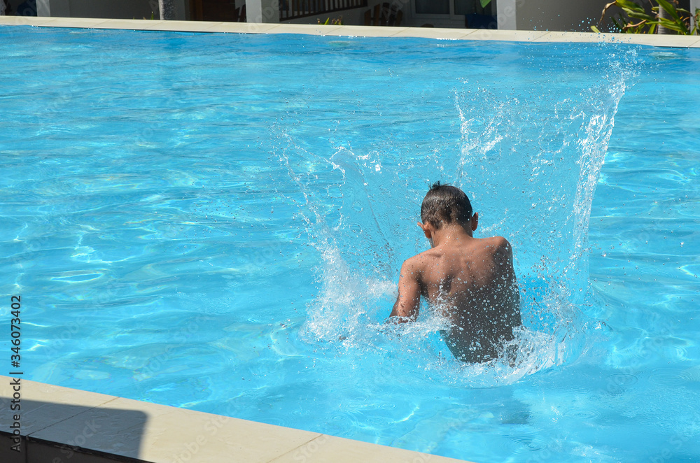 Happy child boy dives in the swimming pool in summer lifestyle back view