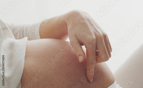 Happy pregnant woman touching her beautiful belly sitting in the bed. Pregnancy, motherhood, and expectation