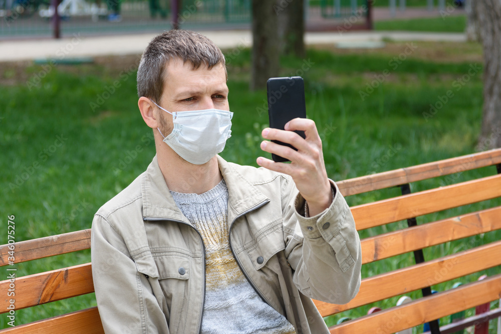 A man in a medical mask sits on a bench and photographs himself A man in a medical mask sits on a bench and photographs himself