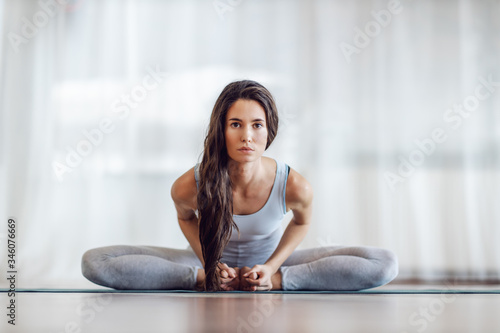 Free Download Attractive yogi brunette sitting on mat in Extended Bound Angle in yoga studio and looking at camera. - GFXLoad