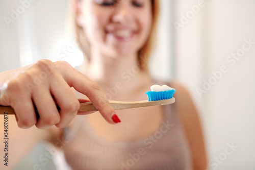 Beautiful smiling caucasian woman standing in bathroom and holding toothbrush with toothpaste. Morning routine. Selective focus on toothbrush.