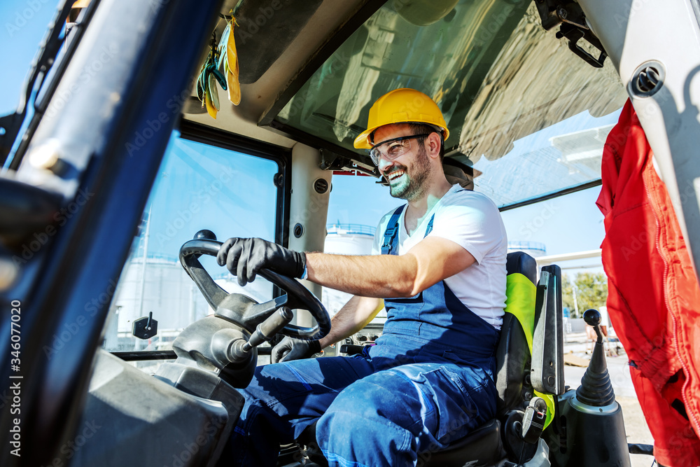 Smiling handsome caucasian worker in overall and with helmet on head driving excavator. Smiling handsome caucasian worker in overall and with helmet on head driving excavator.
