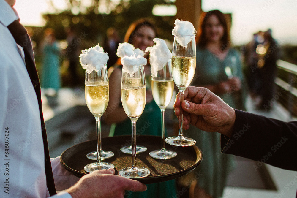 Champagne flutes topped with cotton candy in golden sunlight being picked up by a wedding guest. Champagne flutes topped with cotton candy in golden sunlight being picked up by a wedding guest.