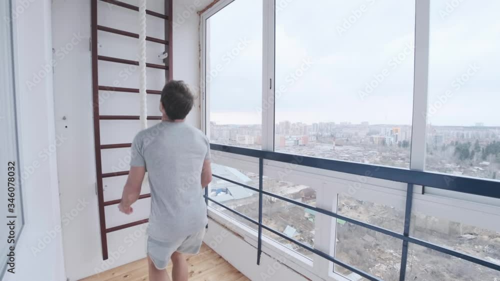 Young man works out on the bright balcony. Man goes out from the room climbs the rope and comes back into the house during home isolation and quarantine, covid19 Young man works out on the bright balcony. Man goes out from the room climbs the rope and comes back into the house during home isolation and quarantine, covid19