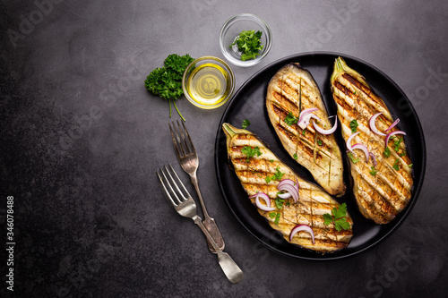 Grilled eggplant slices, garnished with fresh herbs, on black background, top view