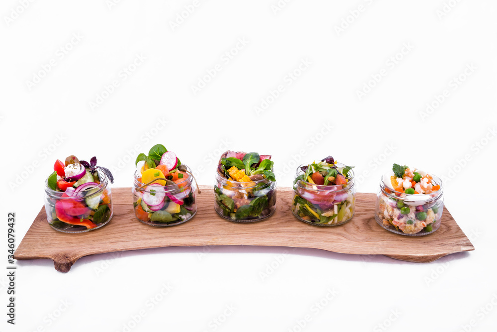 Salads in portioned jars on a wooden tray. Trendy salad in cans. The object is isolated on a white background.