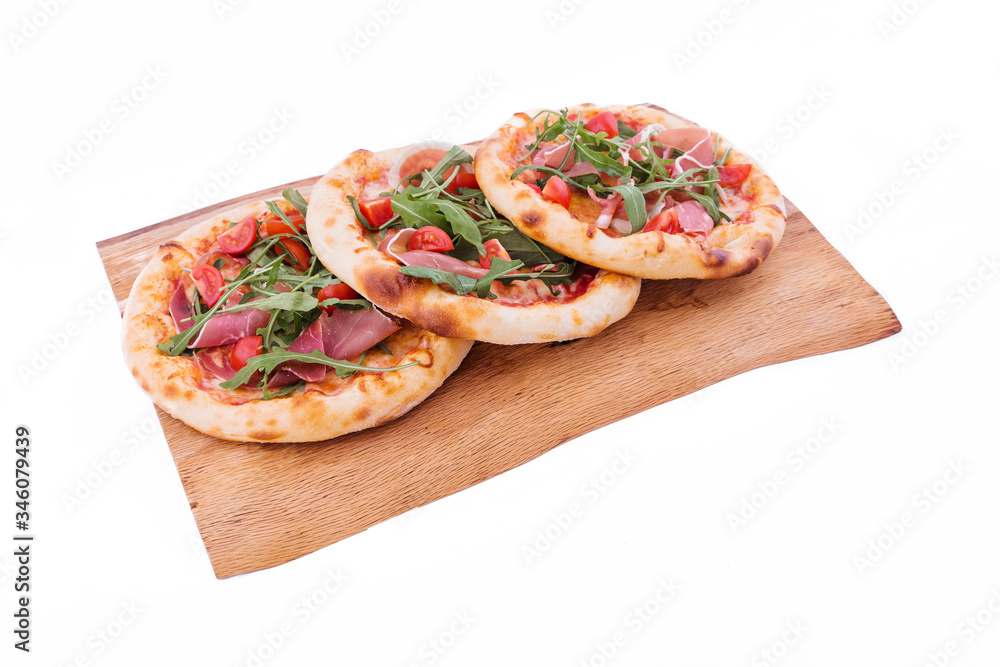 Three pizzas with ham, tomatoes, arugula on a wooden tray. The object is isolated on a white background. Three pizzas with ham, tomatoes, arugula on a wooden tray. The object is isolated on a white background.