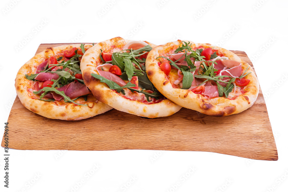 Three pizzas with ham, tomatoes, arugula on a wooden tray. The object is isolated on a white background. Three pizzas with ham, tomatoes, arugula on a wooden tray. The object is isolated on a white background.