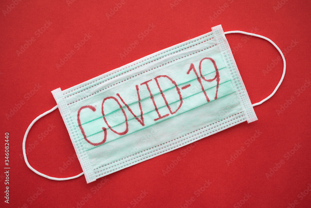 Text COVID-19 on green surgical face mask on red background with copy space. Global novel coronavirus (Covid-19) outbreak pandemic around the world concept. Covid-19 virus spread to China, US, Europe. Text COVID-19 on green surgical face mask on red background with copy space. Global novel coronavirus (Covid-19) outbreak pandemic around the world concept. Covid-19 virus spread to China, US, Europe.