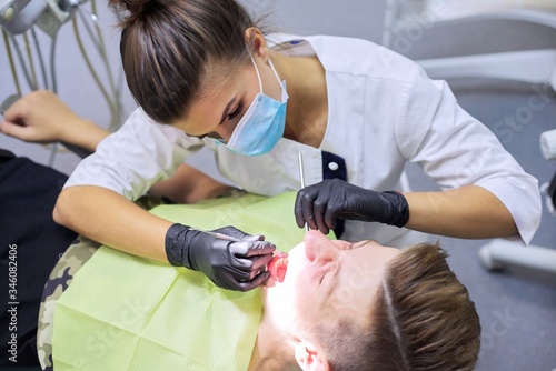 Female dentist treating teeth to patient, young man in chair at dental clinic