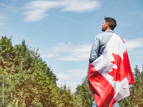 Attractive man holding Canadian Flag on blue sky background on a clear, sunny day. View from the back, close-up. National holiday concept photo