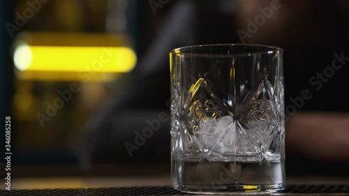 glass on bar,ice cubes fall into glass,bokeh,bartender puts ice and takes glass of Bourbon,whiskey.order at bar,splashes of alcohol,concept alcohol,bar.Close-up, 4k