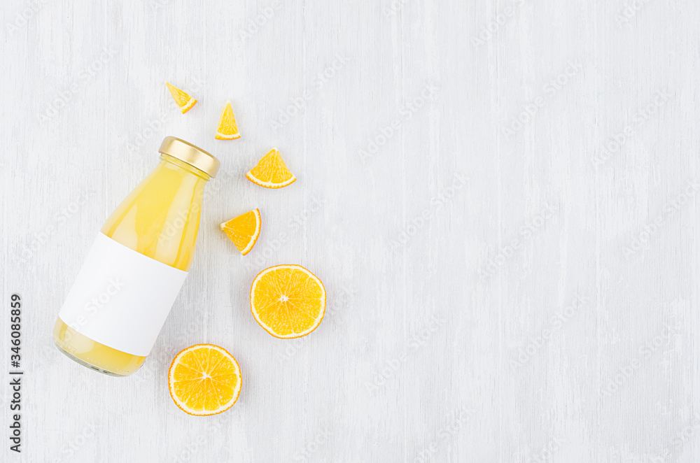 Organic yellow orange juice in glass bottle with sliced fruit, blank label on white wooden background, top view, copy space, mock up for design, advertising. Organic yellow orange juice in glass bottle with sliced fruit, blank label on white wooden background, top view, copy space, mock up for design, advertising.