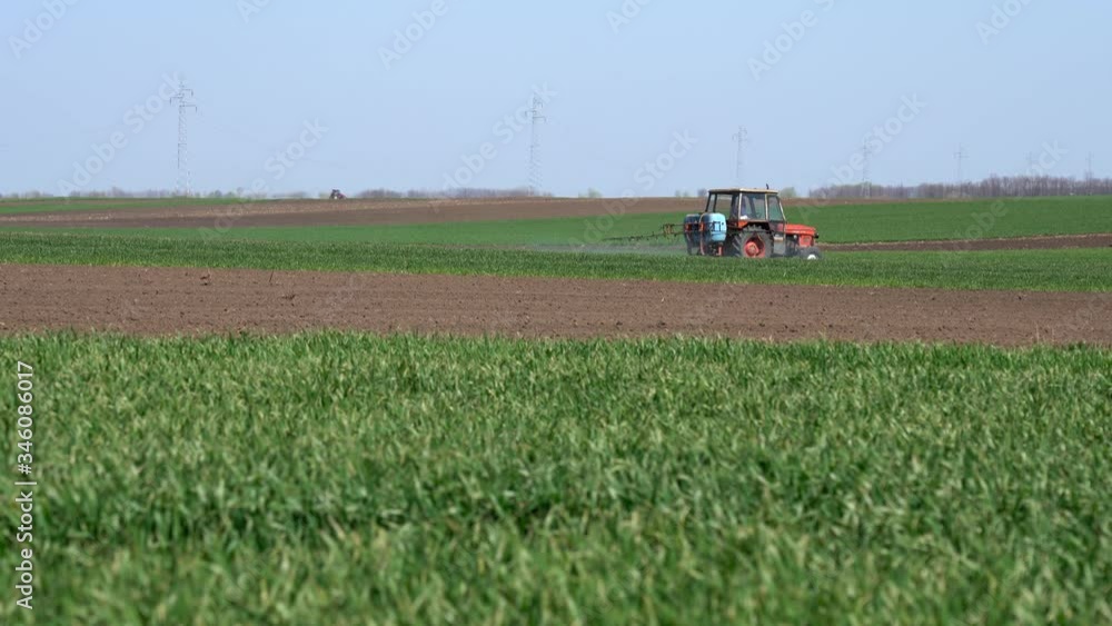 Farming Tractor Spraying Wheat Field in Springtime - Waving Green Wheat Filed with Tractor Sprayer Farming Tractor Spraying Wheat Field in Springtime - Waving Green Wheat Filed with Tractor Sprayer