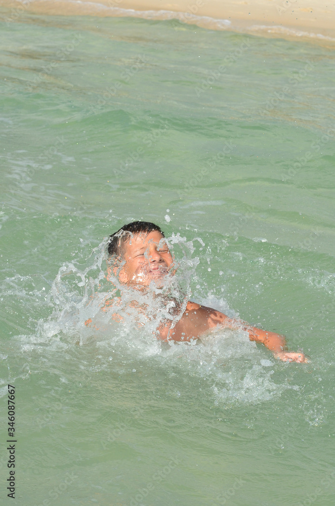 A happy caucasian child is swimming in the sea on summer vacation. A boy in a splash of water on a sunny day lifestyle