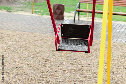 Empty swing at the playground in the rain. Children's swing in the park, wooden benches, slides, sports equipment. Empty city, quarantine.