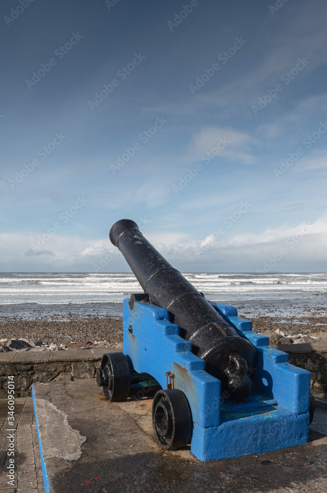 Old cast metal iron cannon by the ocean, Black gun barrel blue carriage. Strandhill beach, county Sligo, Ireland, Cloudy sly over Atlantic ocean. Nobody.