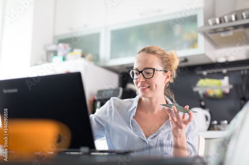 Stay at home and social distancing. Woman in her casual home clothing working remotly from kitchen dining table. Video chatting using social media with friend, family, business clients or partners. photo