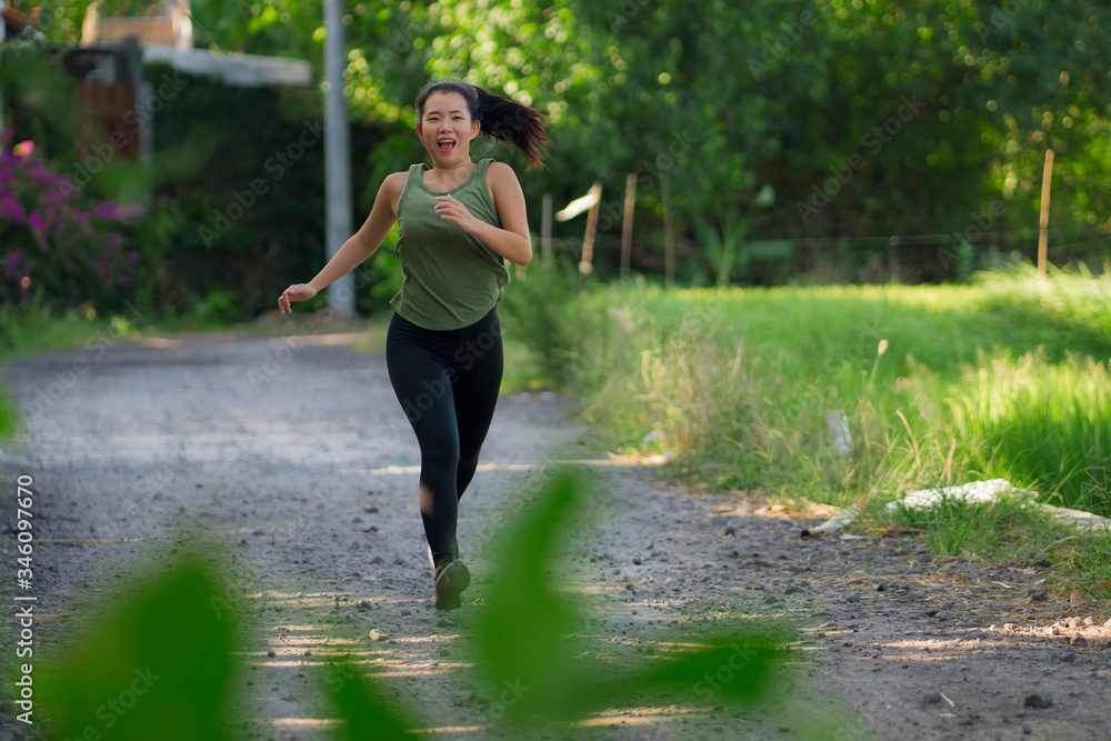 outdoors running workout - young happy and dedicated Asian Chinese woman jogging at beautiful city park or countryside trail on sunset enjoying fitness in healthy lifestyle