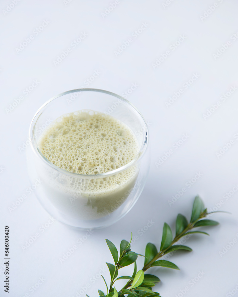 fresh matcha tea in a clear glass with flowers on blue background. Trendy diet drink fresh matcha tea in a clear glass with flowers on blue background. Trendy diet drink