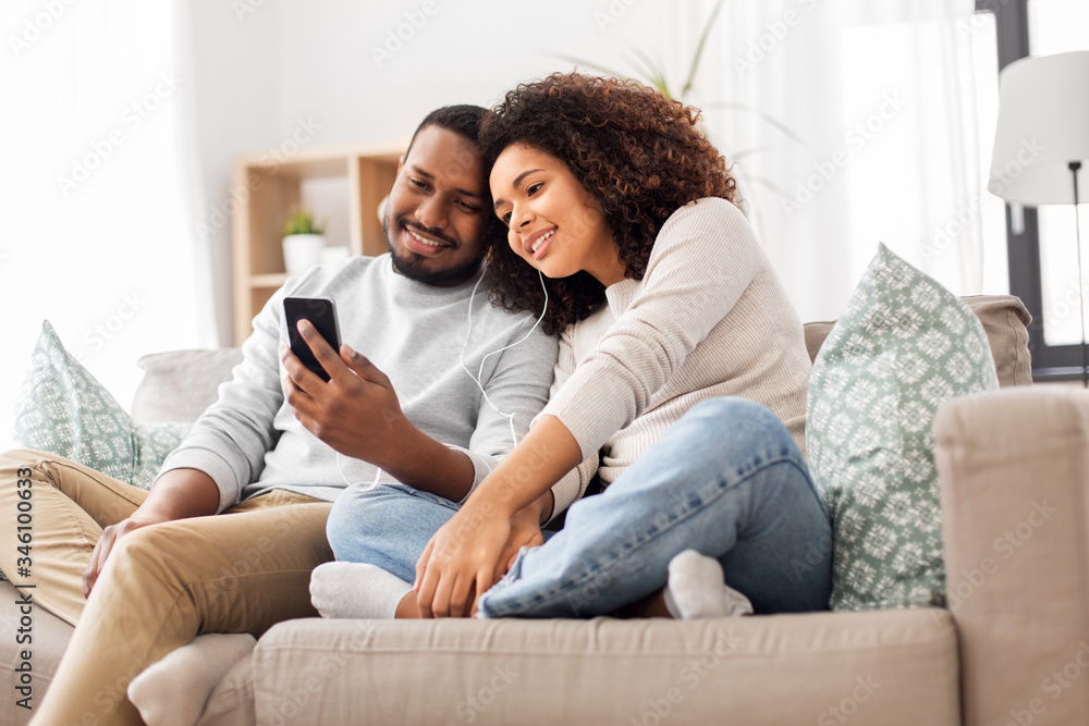 technology, music and people concept - happy african american couple with smartphone and earphones at home