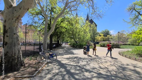 Young mother walking with pram in park. Woman with baby-carriage in citypark and man wears facemask. Covid time