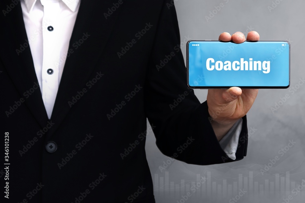 Coaching. Geschäftsmann im Anzug hält ein Smartphone in die Kamera. Der Begriff Coaching steht auf dem Handy. Konzept für Business, Finanzen, Statistik, Analyse, Wirtschaft