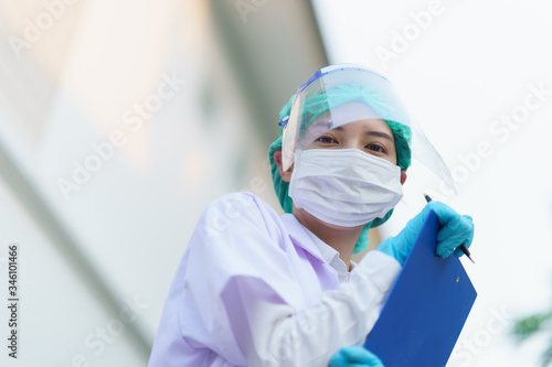 Woman doctor, holding patient report form folder, outdoor portrait, Coronavirus COVID-19 pandemic.
