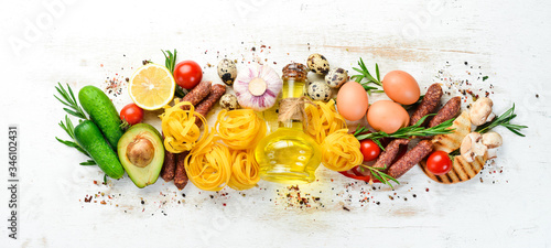 Food background. Dry pasta, tomatoes, spices and vegetables on a white wooden background. Top view.