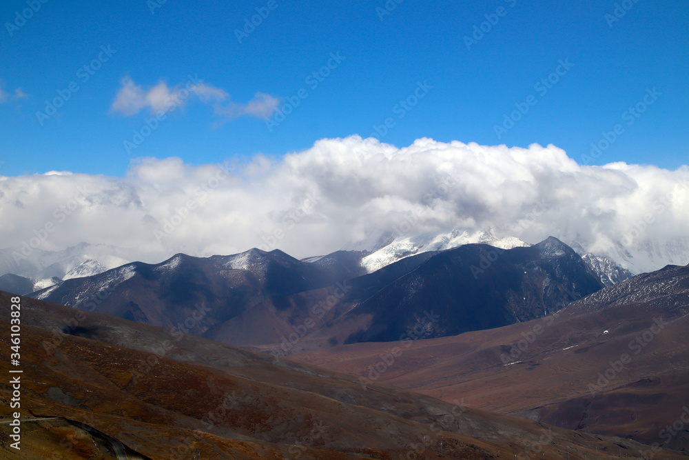 Plateau winding road, blue sky and white clouds, snowy mountains in the distance