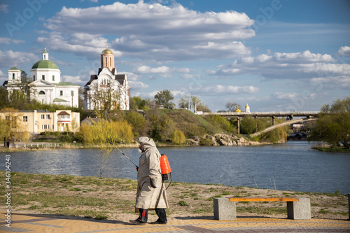 Bila Tserkva, Ukraine - April 20, 2020: A man in a gray coat treats the area with a cleaning solution. Shops, trash cans processing from Covid-19. The Covid-19 Epidemic. Pandemic. Beach. River.