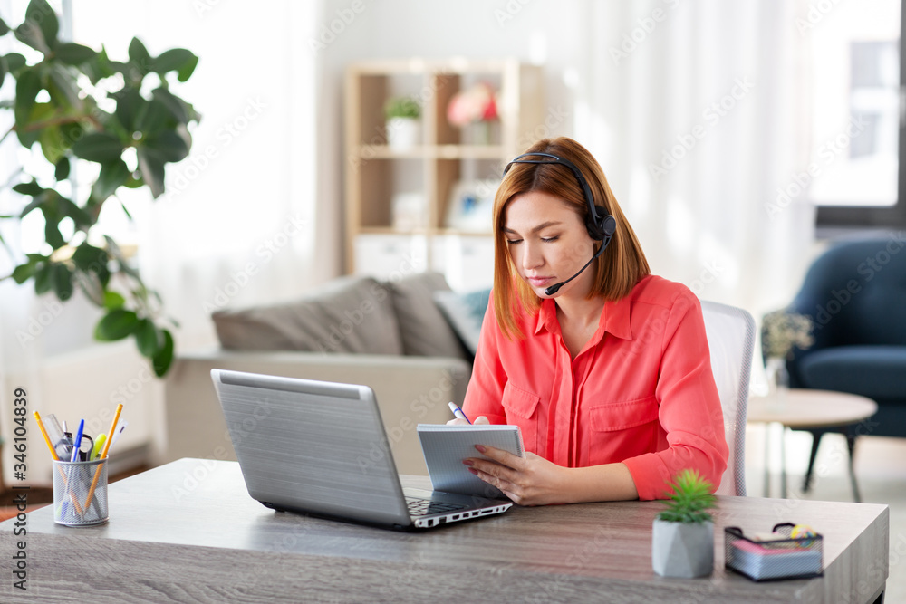 remote job, technology and people concept - young woman with headset and laptop computer having video conference and taking notes to notebook at home office remote job, technology and people concept - young woman with headset and laptop computer having video conference and taking notes to notebook at home office