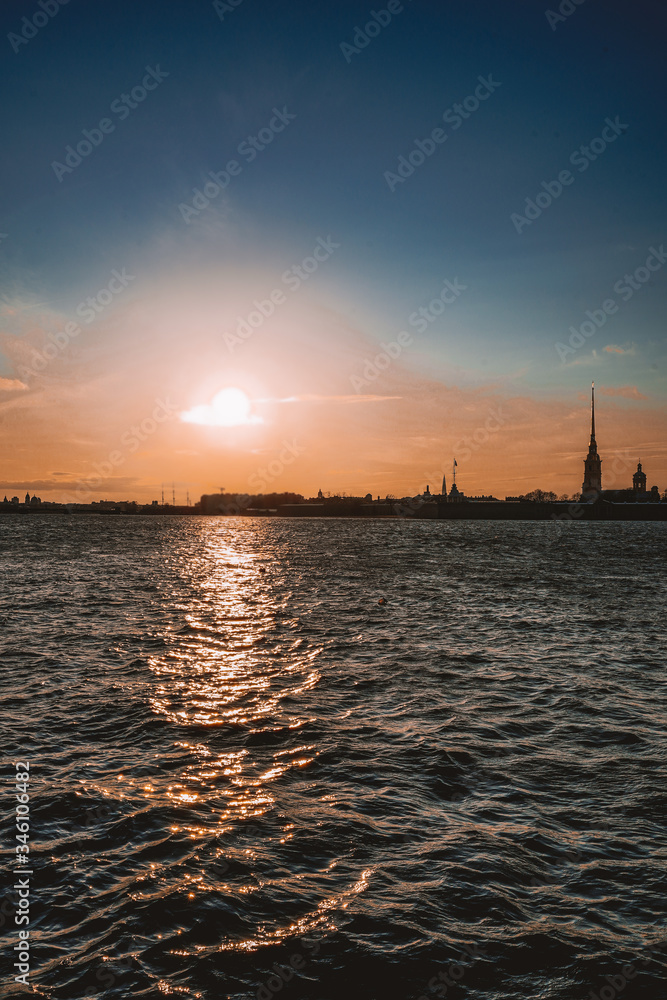 Naklejka premium Granite embankment in Saint Petersburg, beautiful orange sun, bright sunset, the Neva river and the Peter and Paul fortress