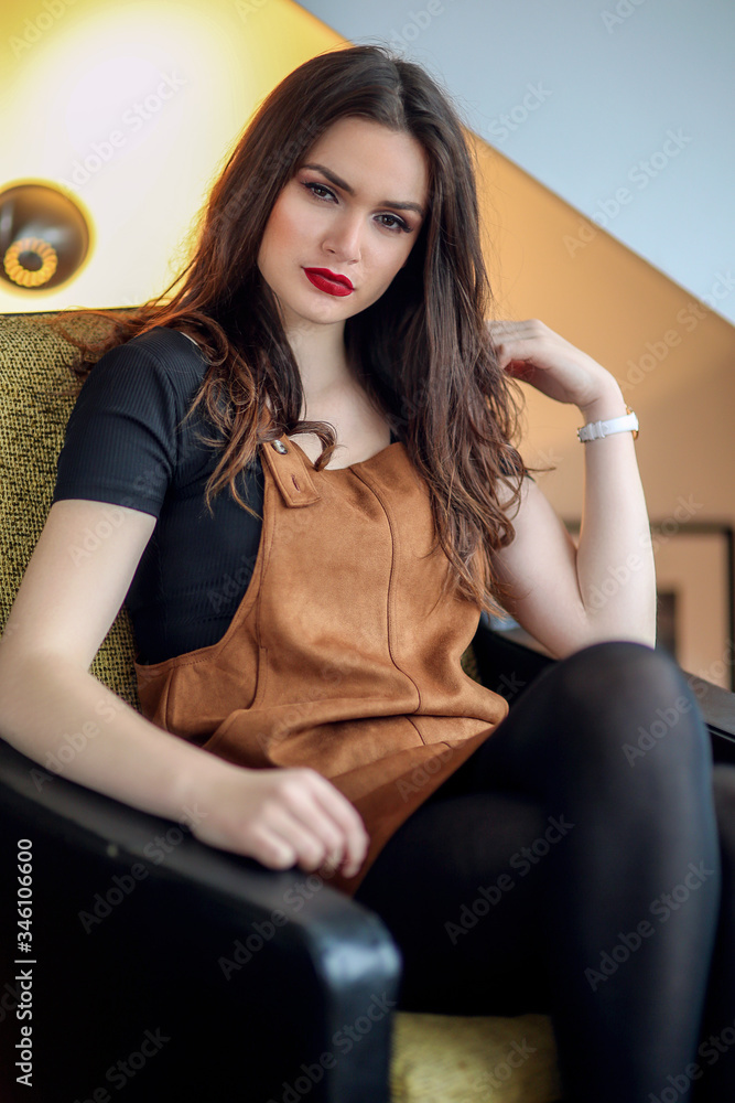 Fototapeta premium Jeune femme assise dans un fauteuil en salopette marron